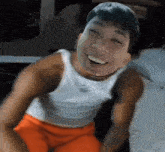 a young man wearing a white tank top and orange shorts is smiling