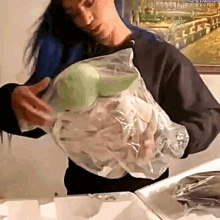 a woman in a black sweatshirt is holding a plastic bag of food