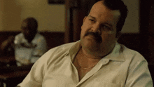 a man with a mustache is sitting at a table in a restaurant and looking at something .