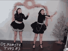 two women are dancing in front of a christmas tree and the words dynamite twins are written on the floor