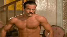a shirtless man with a mustache is standing in front of a staircase .