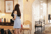 a woman in a blue dress is standing in a room with a picture on the wall that says " things that make me happy "