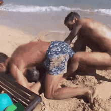 two men are playing in the sand on the beach and one of them is wearing blue shorts