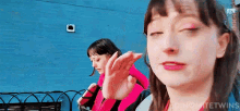 a woman in a pink jacket is standing next to another woman in front of a blue wall ..