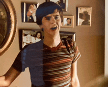 a young man in a striped shirt is standing in front of a wall of framed pictures