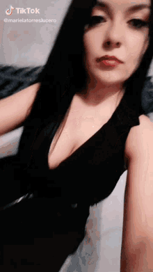 a woman in a black dress with a plunging neckline is taking a selfie on tiktok