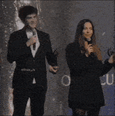 a man in a suit stands next to a woman holding a microphone with the hashtag efnaz_h on the bottom