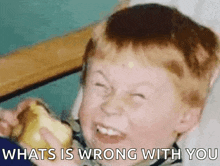 a young boy is eating a banana and making a funny face with the words what 's wrong with you written below him .