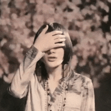 a woman covering her eyes with her hand in front of a tree with flowers
