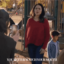 a woman in a red sweater stands in front of a playground with the words " you better watch your mouth " on the bottom