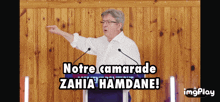 a man stands at a podium with the words notre camarade zahia hamdane