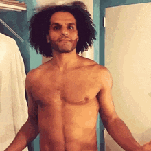 a shirtless man with curly hair is standing in front of a closet with his arms outstretched .