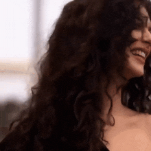 a close up of a woman 's face with long curly hair smiling .