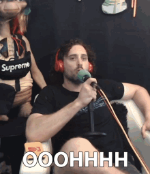 a man wearing headphones and a shirt that says supreme holds a microphone