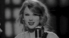 taylor swift is smiling while singing into a microphone in a black and white photo .