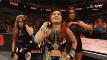 a woman with red hair is standing in a wrestling ring with two other women .