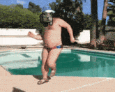 a man in a bathing suit and hat is running by a swimming pool