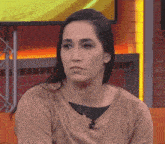 a woman wearing a gold sweater and a gold necklace is looking at the camera