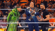 a man in a green robe is standing in a wrestling ring with two men .
