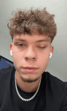 a close up of a man 's face with his eyes closed and a pearl necklace around his neck
