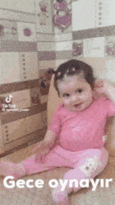 a baby girl in a pink shirt is sitting on the floor with the words " gece oynayir " written below her