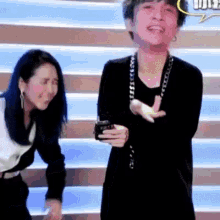 a man and a woman are standing next to each other on a stage and the man is holding a cell phone .
