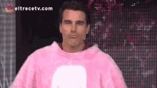 a man in a pink sweater is standing in front of a eltrecetv.com screen