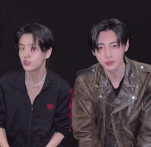 two young men in leather jackets are standing next to each other and holding glasses .