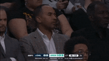 a man in a suit sits in the stands watching a basketball game with espn on the screen behind him