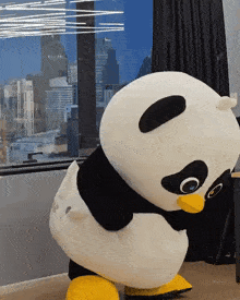 a stuffed panda bear is standing in front of a window with a city in the background