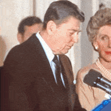 a man in a suit and tie stands next to a woman holding a microphone