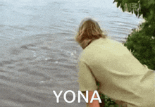 a man is standing next to a body of water and the word yona is on the bottom of the image