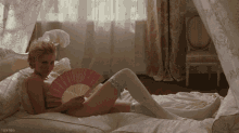 a woman is laying on a bed holding a fan and the word teennoir is on the bottom of the image