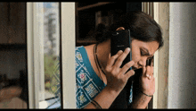 a woman is talking on an oppo phone while looking out a window