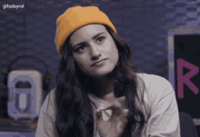 a woman wearing a yellow beanie and a white shirt has the gifsdayrol watermark on the bottom right