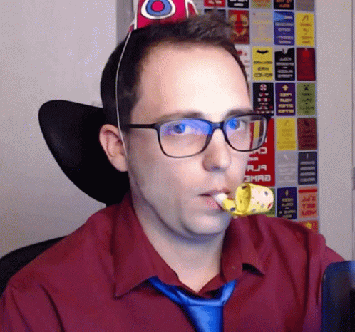 a man wearing glasses and a party hat is holding a party horn in his mouth