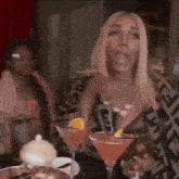 a woman is sitting at a table with two martini glasses and talking .
