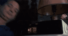 a man is covering his face while looking at a clock that says 6:00