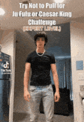 a young man in a black shirt and jeans is standing in front of a refrigerator in a room .