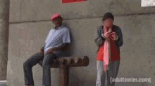 a man sitting on a bench next to a woman looking at her phone