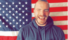a man in front of an american flag laughs with his eyes closed