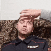 a man in a police uniform is laying on a couch and someone is touching his forehead