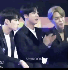 a group of young men are sitting in a dark room and one of them is clapping his hands .