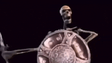 a skeleton is holding a sword and shield in the dark .