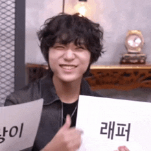a young man with curly hair is smiling and holding a piece of paper with chinese writing