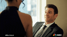 a man in a suit and tie is talking to a woman in a black dress with #suitsla on the bottom