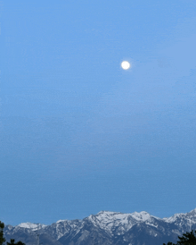 a full moon is rising over a snow covered mountain range