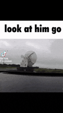 a truck with a large satellite dish on the back is driving down a road with the caption look at him go