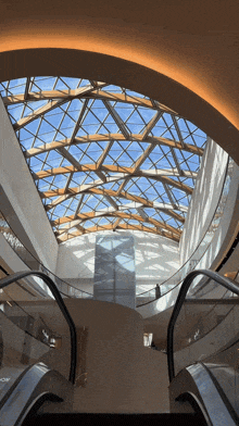 an escalator going up to a ceiling with a blue sky behind it