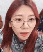 a woman with red hair and glasses is looking at the camera .